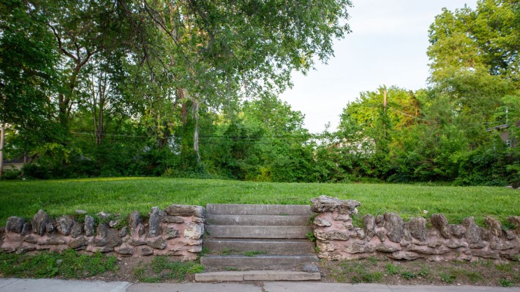 A small stairway leading from the sidewalk up to an empty lawn with a short retaining wall.