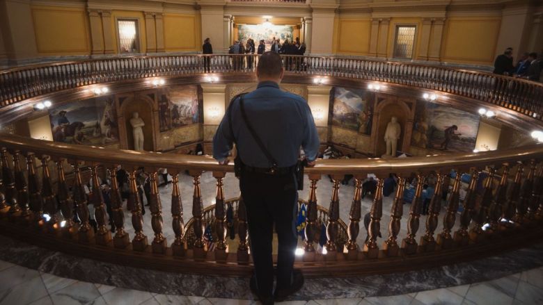 A law enforcement officer stands in the Kansas Statehouse looking down at people walking through the halls.