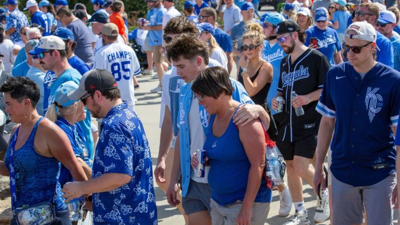 A crowd of Royals fans, dressed in blue and in team merchandise, walking across the parking lot at Kauffman Stadium.