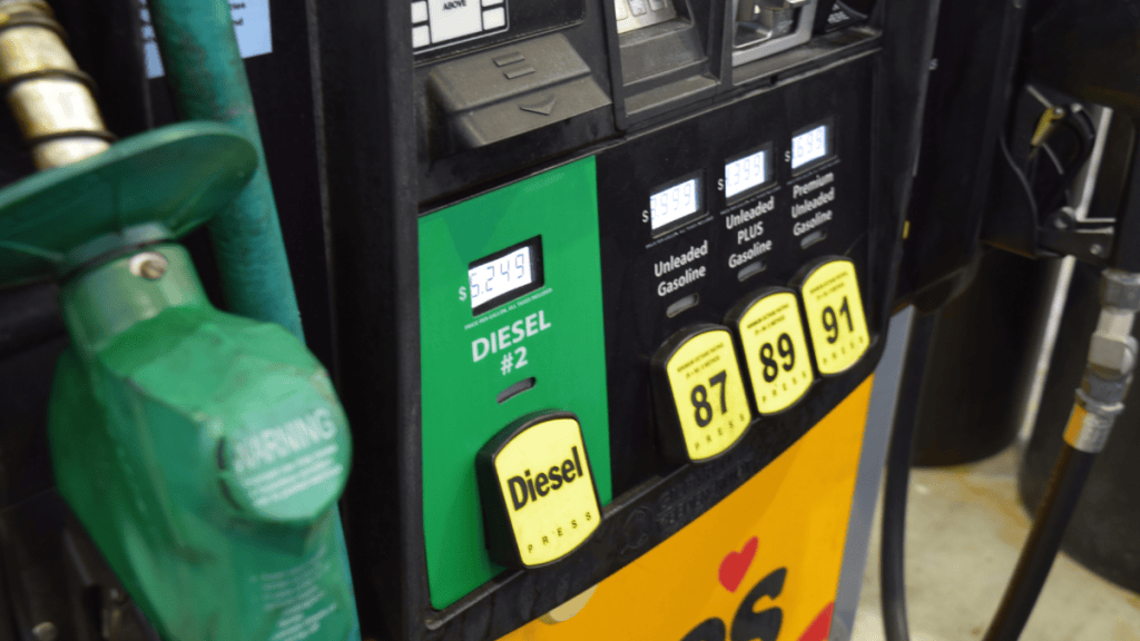 Close-up of a fuel pump with a green panel labeled "Diesel #2" showing a price of $6.249 per gallon, beside a green diesel nozzle and yellow buttons for 87, 89 and 91 octane gasoline.