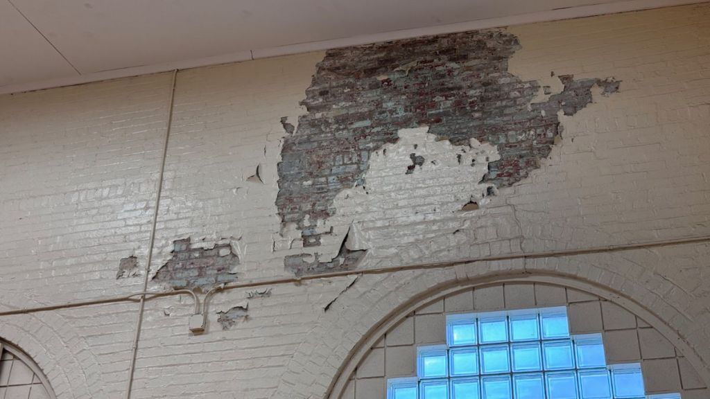 A brick wall, painted white, with a large section flaking off above a window.